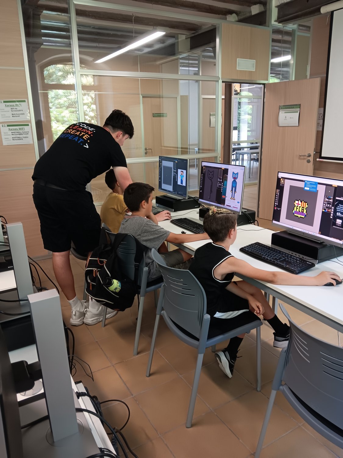 Un mentor de Pixel Penedès ajudant tres alumnes amb el seu projecte de disseny de personatges a l'ordinador